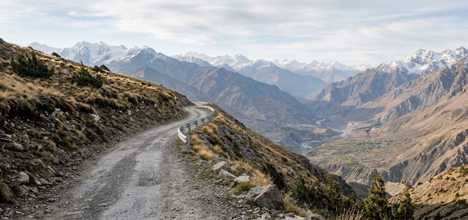Mountain road revealing a valley and distant Himalayan landscape during a journey